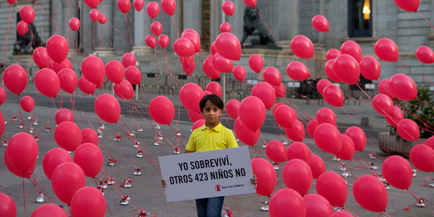 Zaid, an 8-year-old Syrian refugee now living in Spain, poses with a sign reading in Spanish: "I survived, 423 other children did not", in front of the Spanish Parliament in Madrid. Picture / AP
