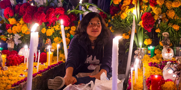 A woman sits by a relative's grave for Dia de los Muertos in Oaxaca. Photo / 123RF