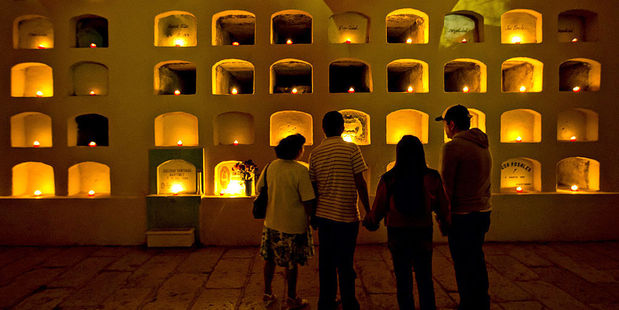 A family pauses to view candles lighting the crypts of San Miguel cemetery in Oaxaca, Mexico. Photo / Getty Images