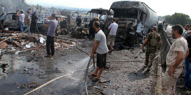 Syrian security forces look at the remains of burned vehicles at the site of a bombing yesterday after multiple bomb blasts struck government and military targets around the country. Photo / SANA