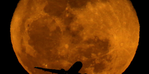 A waning moon rises in the distance as a passenger jet takes off. Photo / AP