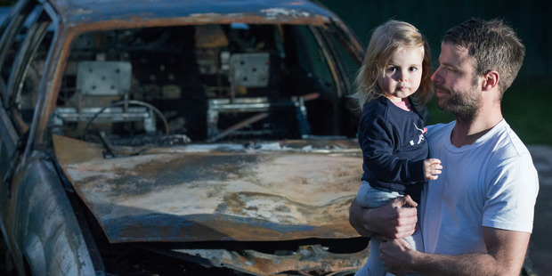 Adam Holt and two-year-old daughter Ava Holt, stand in front of Holt's burnt out 1987 Holden Calais that caught fire while Holt was driving down Auckland's Pakuranga Highway. Photo / Nick Reed