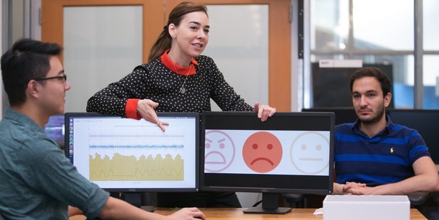 Professor Dina Katabi explains how PhD student Fadel Adib's (right) face is neutral but that EQ-Radio's analysis of his heartbeat and breathing show that he is sad. Photo: Jason Dorfman/MIT CSAIL