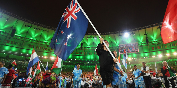 Gold and silver medalist Liam Malone carries the New Zealand flag during the closing ceremony. Photo / Getty Images