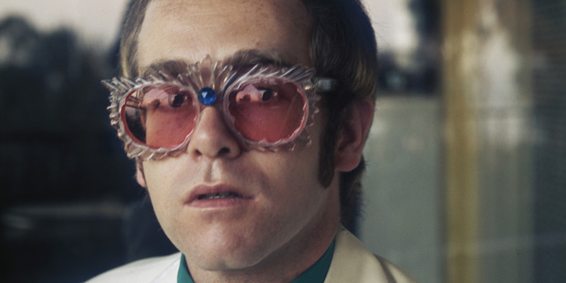 English pop singer Elton John in a white jacket and rococco spectacles during a photoshoot at his home for his 1974 Greatest Hits album, 1974. Photo / Getty