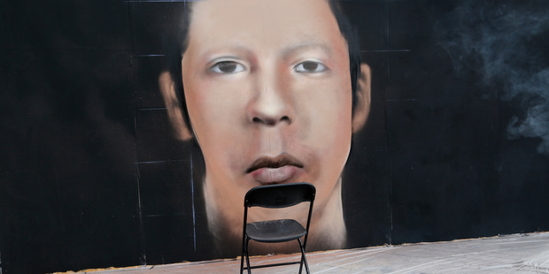 An empty folding chair stands next to a mural depiction of a missing young man during a demonstration in Mexico City today. Photo / AP