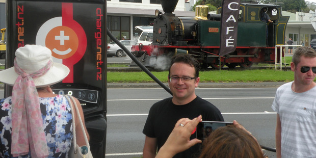 The steam train on Kawakawa's main road provides a historical backdrop to 21st-century technology, as FastNet's Steve West poses for a photo. Photo / Peter Shand