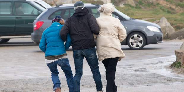 A man helps his companions to walk in the wind in Newquay. Photo / Getty Images