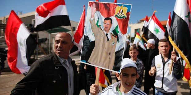 Druze residents of the Buqata village in the Israeli annexed Golan Heights wave Syrian flags and a placard depicting a portrait of Syrian President Bashar al-Assad. Photo / AFP