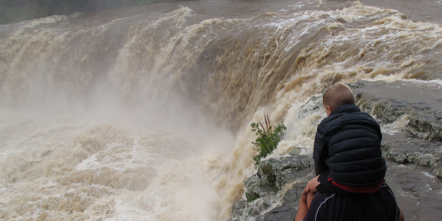 A father and son watched a flood-swollen Haruru Falls on the Waitangi River, inland from Paihia today. Photo/Peter de Graaf