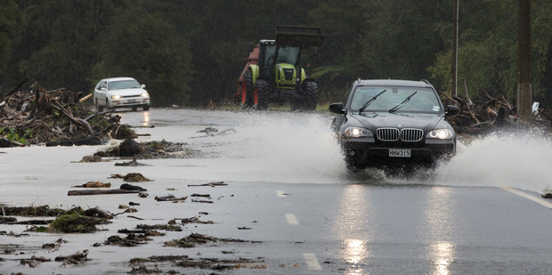 Vehicles slowly make their way through debris and floodwater on State Highway 25 near Whangamata during last week's flooding. Photo / Alan Gibson
