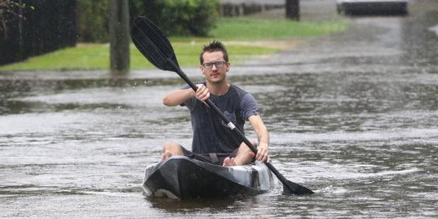 Harrison Orth paddles down the flooded Corella St in Rocklea, Brisbane. Photo / Darren England, News Corp Australia