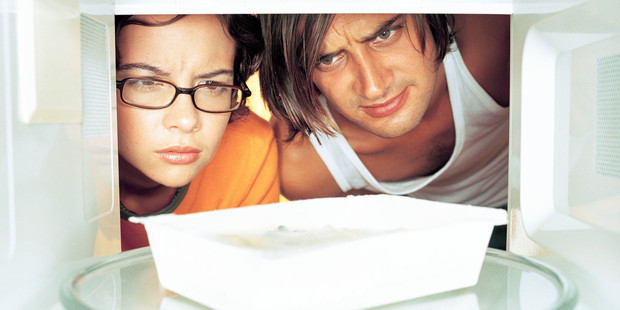 Young man and woman looking at microwave meal in microwave