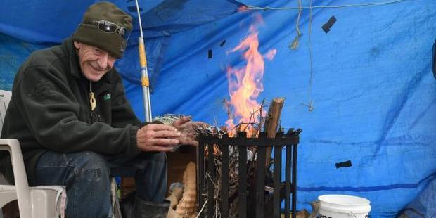 John Carvalho warms his hands at an open fire as wind and rain buffet his whitebait camp near Henley yesterday. Photo: Gregor Richardson