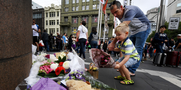 A child lays flowers on the corner of Bourke and Elizabeth Streets. Photo / AAP