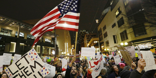 A protester waves a U.S. flag as another holds a sign that reads "Let Them In" during a march and rally to oppose President Donald Trump. Photo / AP