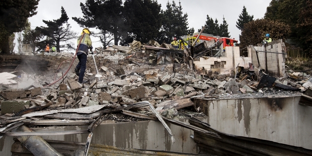 Firefighters spray water on the smouldering ruins of homes on the Port Hills. Photo / Alan Gibson