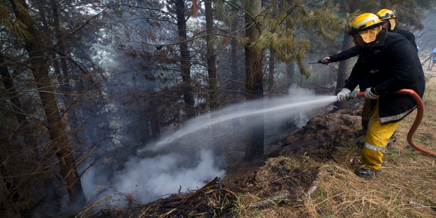 Firefighters spray water on the smouldering ground at the Port Hills. Photo / Alan Gibson