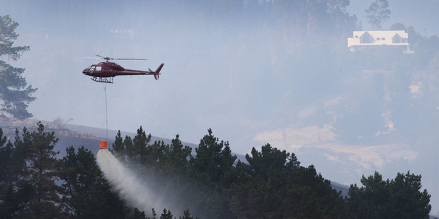 A helicopters uses a monsoon bucket to douse the bushfires still raging in the Port Hills above Christchurch today. Photo / Alan Gibson.