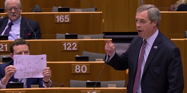 UK Labour MEP Seb Dance, left, holds up a sign as UK Independence Party MEP Nigel Farage addresses the European Parliament. Photo / AP)