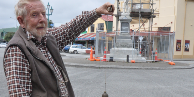 Max Dowell lines up a plumb-bob to check the level of Hokitika's pioneer statue, which he believes is slumping slightly to the south-east. Photo / Janna Sherman
